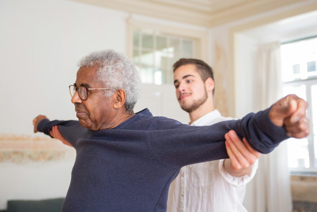 A senior man is assisted by a Physiotherapist for stretching exercises indoors.